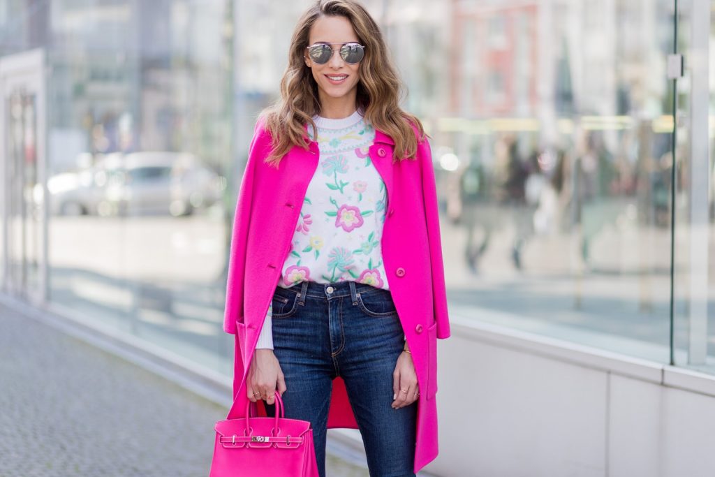 Model and fashion blogger Alexandra Lapp wearing a cashmere pullover from Heartbreaker with precious details of sewed on colorful pastel flowers, slim fit high waist denim from Rag & Bone, a pink wool and cashmere coat by Prada, turquoise pumps with a silver tip from Manolo Blahnik, Le Specs sunglasses and the Mini Birkin bag in electric pink and calf leather with fold-over closure from Hermes on March 30, 2017 in Duesseldorf, Germany.