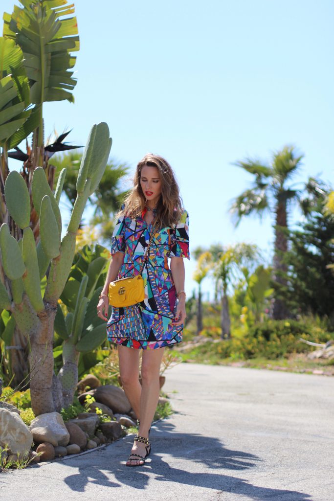 Malibu, Los Angeles; Model and fashion blogger Alexandra Lapp wearing a colorful dress by La Martina, the Polo brand, sandals from Saint Laurent in black with golden rock studs, red lipstick from MAC, a yellow Gucci GG Marmont bag, IWC Da Vinci Automatic 36 watch in 18-carat red gold with diamonds and jewelry from AYS (Art Youth Society) in Malibu on April 17, 2017 in Los Angeles, California.