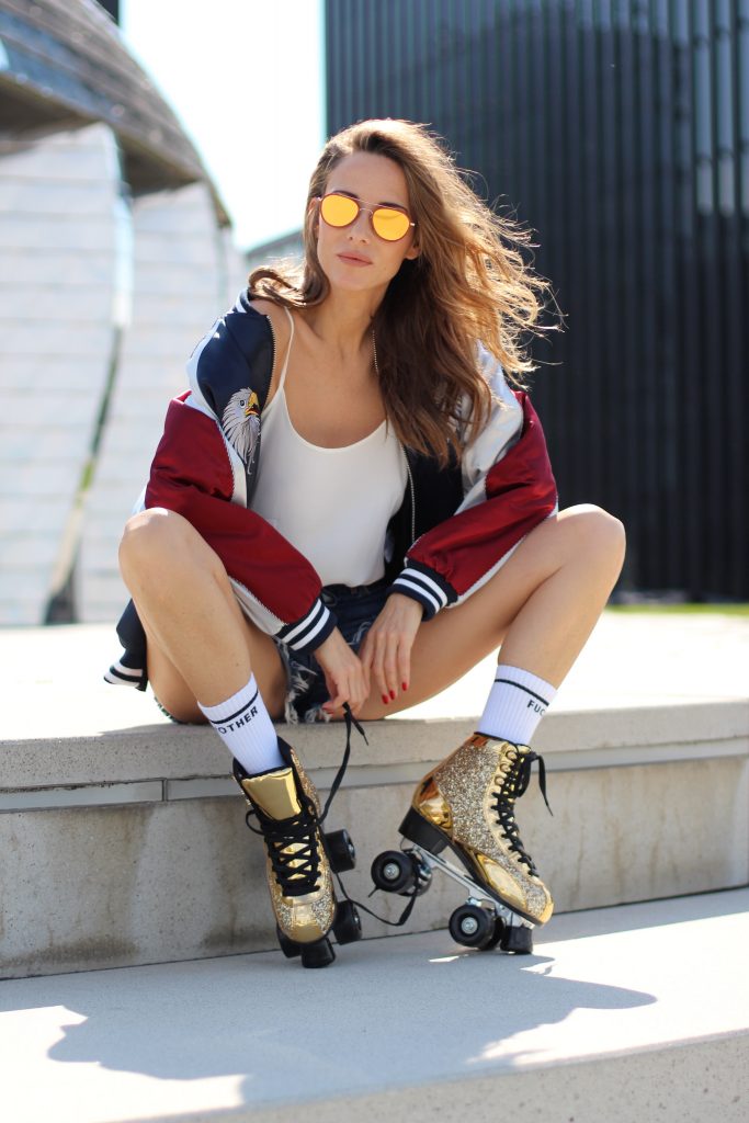 Model and Blogger Alexandra Lapp wearing golden, sparkling Roller Skates from Cosmoparis, mother-fucker socks from Mother Denim, Jadicted silk top in white, Levi's fringed denim high waist shorts, Stylenanda bomber jacket with an embroidered eagle and the letters 'Nothing is impossible' on the back of the three tone jacket in blue, white and red & Thom Browne aviator sunglasses in gold with red, in Duesseldorf on June, 2017.