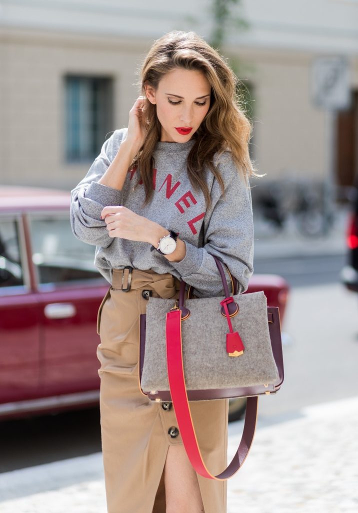 Alexandra Lapp (model, blogger) wearing a vintage sweater from Chanel in grey melange, printed with Chanel red capital letters, a red lipstick and a powder box from Chanel, a midi skirt in a trench silhouette from Self-Portrait, with beige cotton and utilitarian buttons, a belt and a asymmetric cut with a thigh-high slit, red Christian Louboutin pumps in crepe de satin, MCM Milla Spanish leather Tote bag and black Celine Audrey sunglasses during the Mercedes-Benz Fashion Week Berlin Spring/Summer 2018 on July 6, 2017 in Berlin, Germany. (Photo by Christian Vierig)