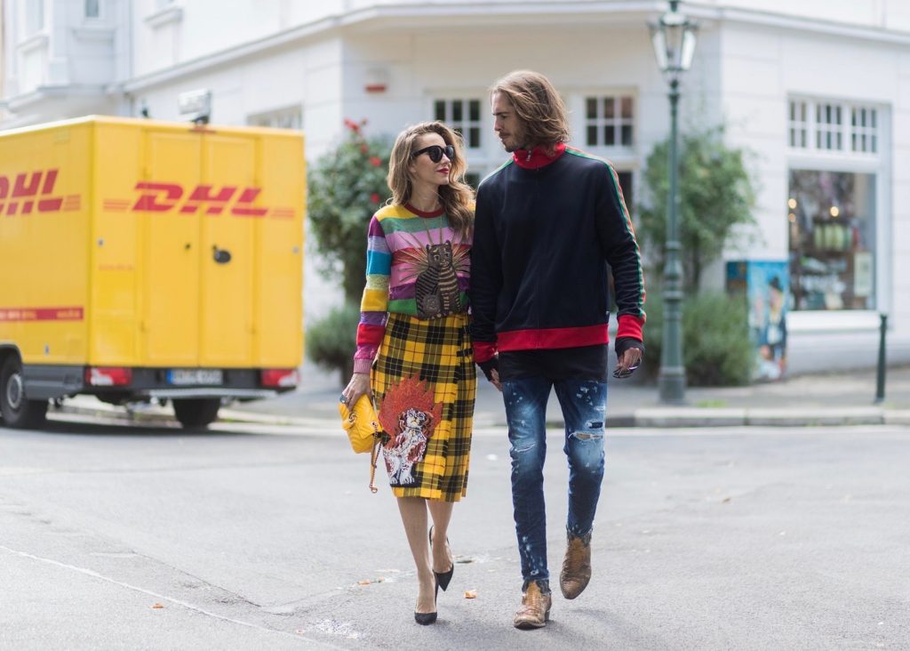 Couple look a like holding hands in front of DHL van - Model and Blogger Alexandra Lapp wearing a Gucci total look, a yellow and red pleated tartan skirt embroidered with a spaniel dog and belt buckle closure, colorful striped sweater with lace and merino with embroidered cat applique all Gucci, black Christian Louboutin So Kate pumps, GG Marmont Gucci bag in yellow, Audrey sunglasses from Celine and Model and Blogger Thomas Stuch wearing classic Kenny Twist Jean from Dsquared, black T-Shirt Thom Krom, Gucci track suit top, Stallion Cowboy Boots on August 4, 2017 in Duesseldorf, Germany.