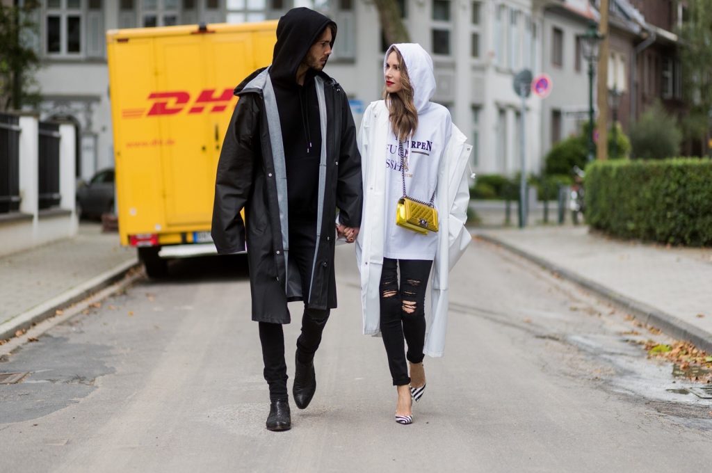 Couple look a like holding arms in front of a DHL van - Model and Blogger Alexandra Lapp wearing oversized Vetements raincoat with a hood in white, Vetements hoodie in white, destroyed Adriano Goldschmied high waist denim in black, black and white So Kate pumps with a yellow heel, yellow golden lacquer Boy bag from Chanel and a big golden ring with baguette diamonds from Schubart Goldschmiede and Model and Blogger Thomas Stuch wearing black oversized raincoat with a hood in black from Vetements, Stella McCartney hoodie in black, Dsquared slim fit denim, Ghost cowboy boots on August 4, 2017 in Duesseldorf, Germany.