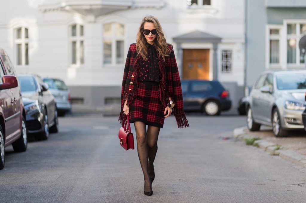 Model and fashion blogger Alexandra Lapp wearing a military jacket in red and black with checkered pattern and frayed sleeves from Balmain, plaid pattern high waist mini skirt by Balmain, red heart intarsia knit by Red Valentino, Celine Box bag in red and red lacquer pumps by Gianvito Rossi, rose gold ring with baguette diamonds on August 4, 2017 in Duesseldorf, Germany.