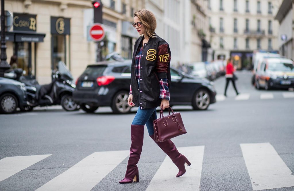 Alexandra Lapp wearing an oversized college jacket in leather from Set Fashion, a plaid shirt with studs from Set, high waist skinny jeans by Rag and Bone, Milla Tote bag with studded outlines in rustic brown from MCM, Les Specs sunglasses, and overknee boots in burgundy by Zara is seen during Paris Fashion Week Spring/Summer 2018 on September 26, 2017 in Paris, France.