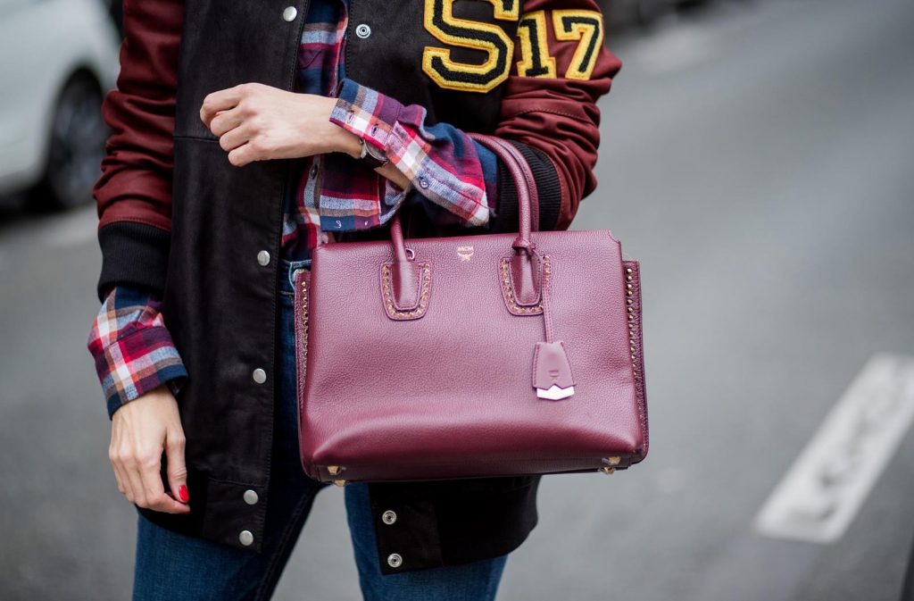 Alexandra Lapp wearing an oversized college jacket in leather from Set Fashion, a plaid shirt with studs from Set, high waist skinny jeans by Rag and Bone, Milla Tote bag with studded outlines in rustic brown from MCM, Les Specs sunglasses, and overknee boots in burgundy by Zara is seen during Paris Fashion Week Spring/Summer 2018 on September 26, 2017 in Paris, France.