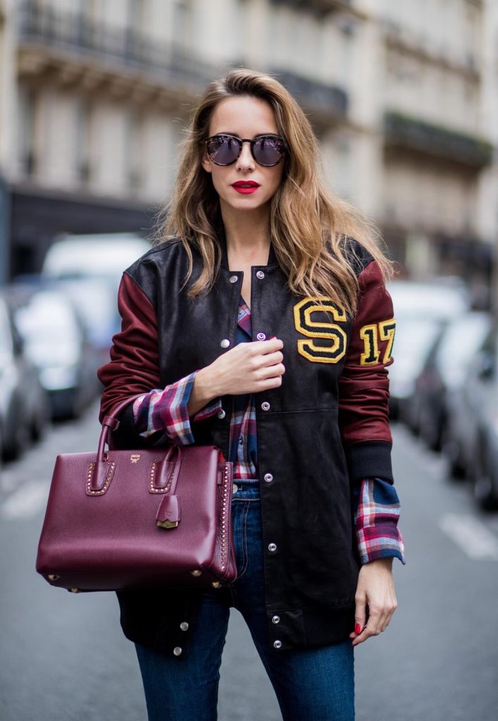 Alexandra Lapp wearing an oversized college jacket in leather from Set Fashion, a plaid shirt with studs from Set, high waist skinny jeans by Rag and Bone, Milla Tote bag with studded outlines in rustic brown from MCM, Les Specs sunglasses, and overknee boots in burgundy by Zara is seen during Paris Fashion Week Spring/Summer 2018 on September 26, 2017 in Paris, France.