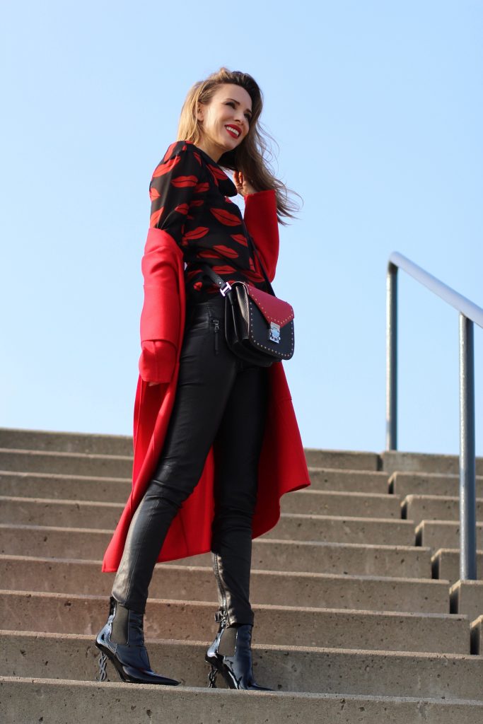 Alexandra Lapp wearing the new MCM Made-To-Order Patricia bag, a Made-To-Order service, giving everyone the opportunity of designing her own personal and unique Patricia bag, black leather pants from Unravel, a silk blouse with red lips from Saint Laurent, a cashmere coat in red from Hermès, black patent ankle boots from YSL, red lipstick by Dior.