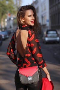 Alexandra Lapp wearing the new MCM Made-To-Order Patricia bag, a Made-To-Order service, giving everyone the opportunity of designing her own personal and unique Patricia bag, black leather pants from Unravel, a silk blouse with red lips from Saint Laurent, a cashmere coat in red from Hermès, black patent ankle boots from YSL, red lipstick by Dior.