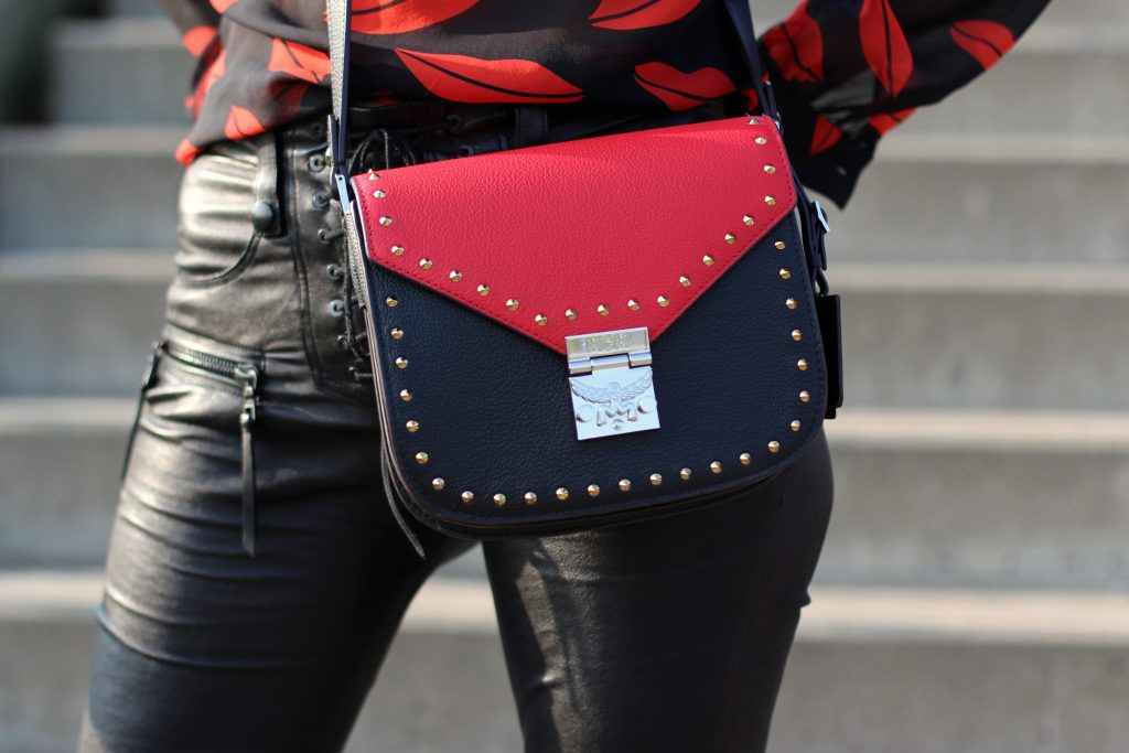 Alexandra Lapp wearing the new MCM Made-To-Order Patricia bag, a Made-To-Order service, giving everyone the opportunity of designing her own personal and unique Patricia bag, black leather pants from Unravel, a silk blouse with red lips from Saint Laurent, a cashmere coat in red from Hermès, black patent ankle boots from YSL, red lipstick by Dior.