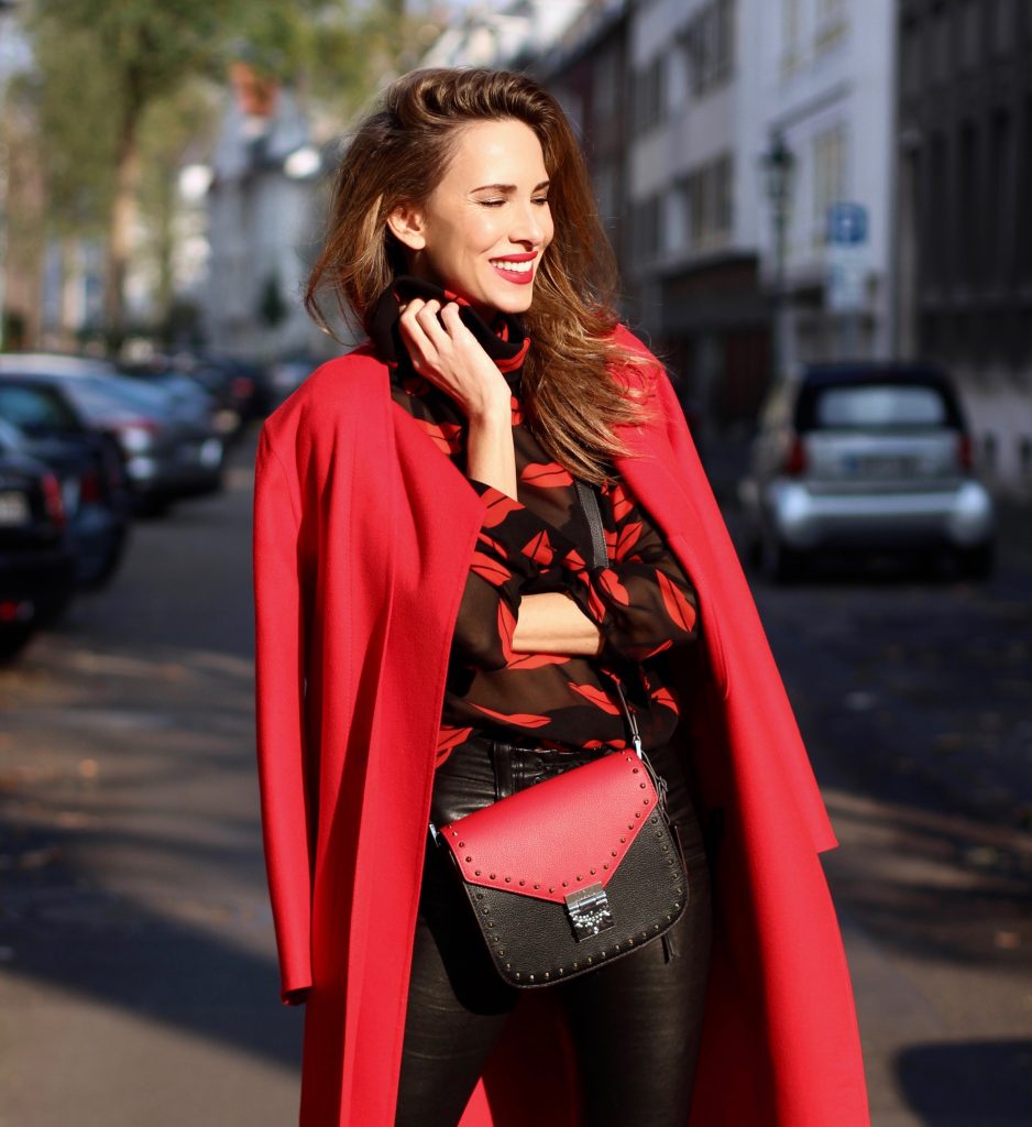 Alexandra Lapp wearing the new MCM Made-To-Order Patricia bag, a Made-To-Order service, giving everyone the opportunity of designing her own personal and unique Patricia bag, black leather pants from Unravel, a silk blouse with red lips from Saint Laurent, a cashmere coat in red from Hermès, black patent ankle boots from YSL, red lipstick by Dior.