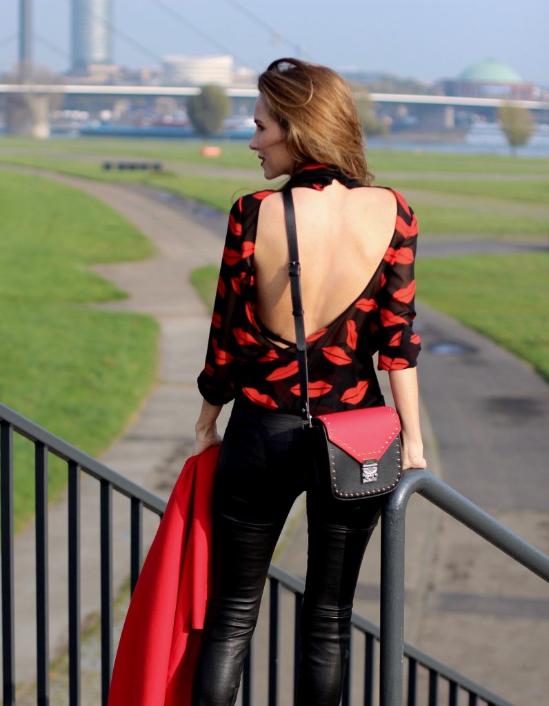 Alexandra Lapp wearing the new MCM Made-To-Order Patricia bag, a Made-To-Order service, giving everyone the opportunity of designing her own personal and unique Patricia bag, black leather pants from Unravel, a silk blouse with red lips from Saint Laurent, a cashmere coat in red from Hermès, black patent ankle boots from YSL, red lipstick by Dior.