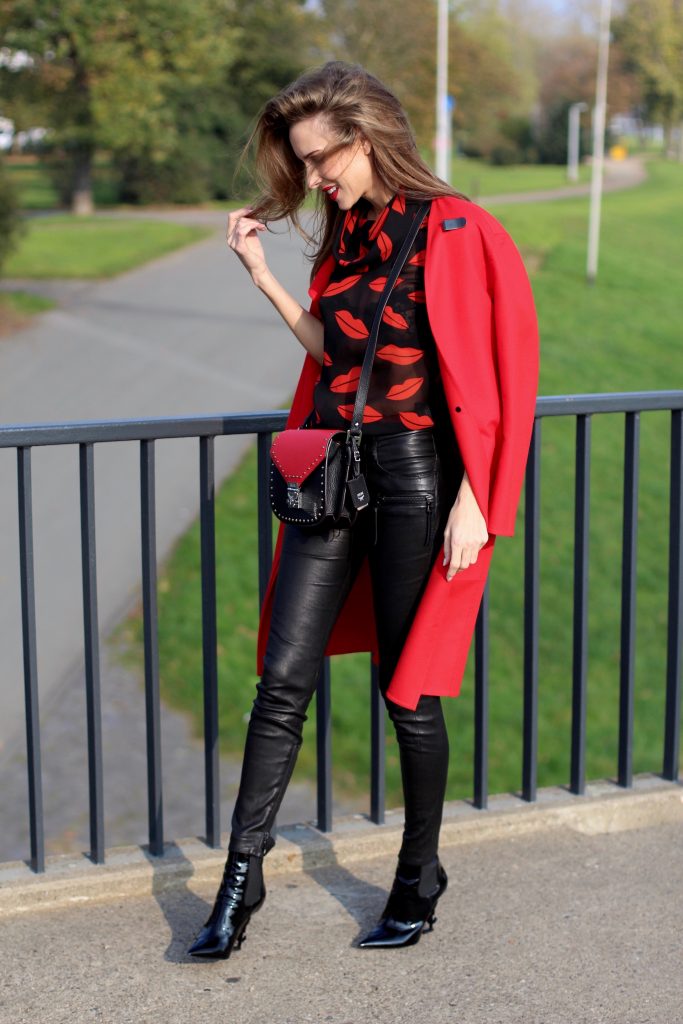 Alexandra Lapp wearing the new MCM Made-To-Order Patricia bag, a Made-To-Order service, giving everyone the opportunity of designing her own personal and unique Patricia bag, black leather pants from Unravel, a silk blouse with red lips from Saint Laurent, a cashmere coat in red from Hermès, black patent ankle boots from YSL, red lipstick by Dior.
