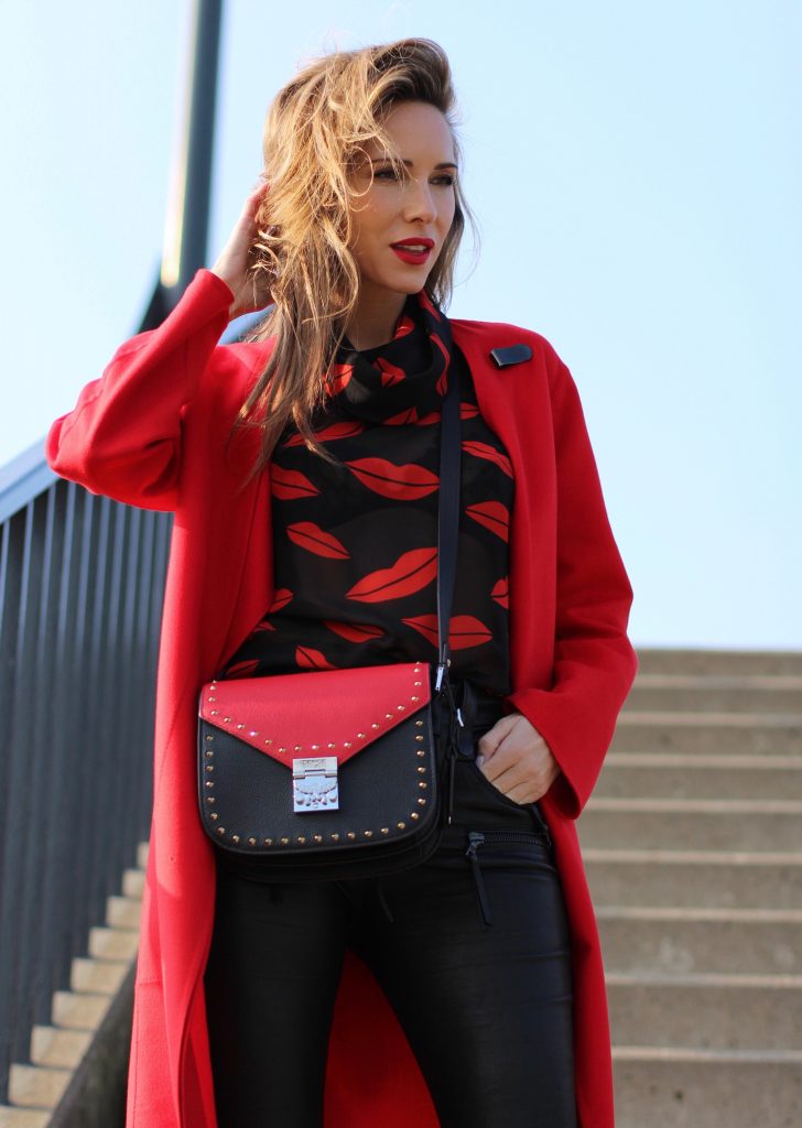 Alexandra Lapp wearing the new MCM Made-To-Order Patricia bag, a Made-To-Order service, giving everyone the opportunity of designing her own personal and unique Patricia bag, black leather pants from Unravel, a silk blouse with red lips from Saint Laurent, a cashmere coat in red from Hermès, black patent ankle boots from YSL, red lipstick by Dior.