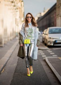 Alexandra Lapp wearing silver pants in leather and biker style by Balmain, long blue silk blouse from Equipment, cashmere pullover in grey with a green dragon application by Heartbreaker, green parka equipped with light blue fur inside, silver mirrored sunglasses by le Specs, Christian Louboutin So Kate heels in neon yellow and the Kate Monogram Chain Grain leather shoulder bag in neon yellow by Saint Laurent is seen during Paris Fashion Week Spring/Summer 2018