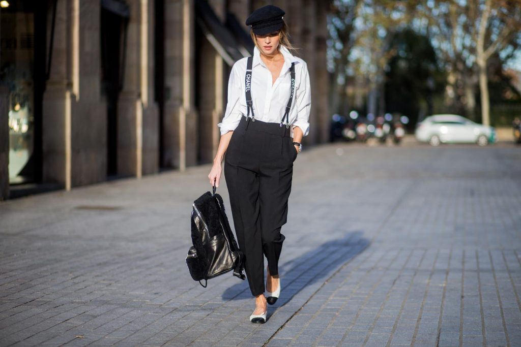 Alexandra Lapp wearing black and white vintage Chanel suspenders with Chanel logo in black and white, a white oversized shirt from Steffen Schraut, black high waist pants from Zara, XL backpack in lambskin with black and white MCM logo and Chanel baker boy cap in black tweed and ballerinas in white with black tip and logo from Chanel on November 27, 2017 in Barcelona, Spain.