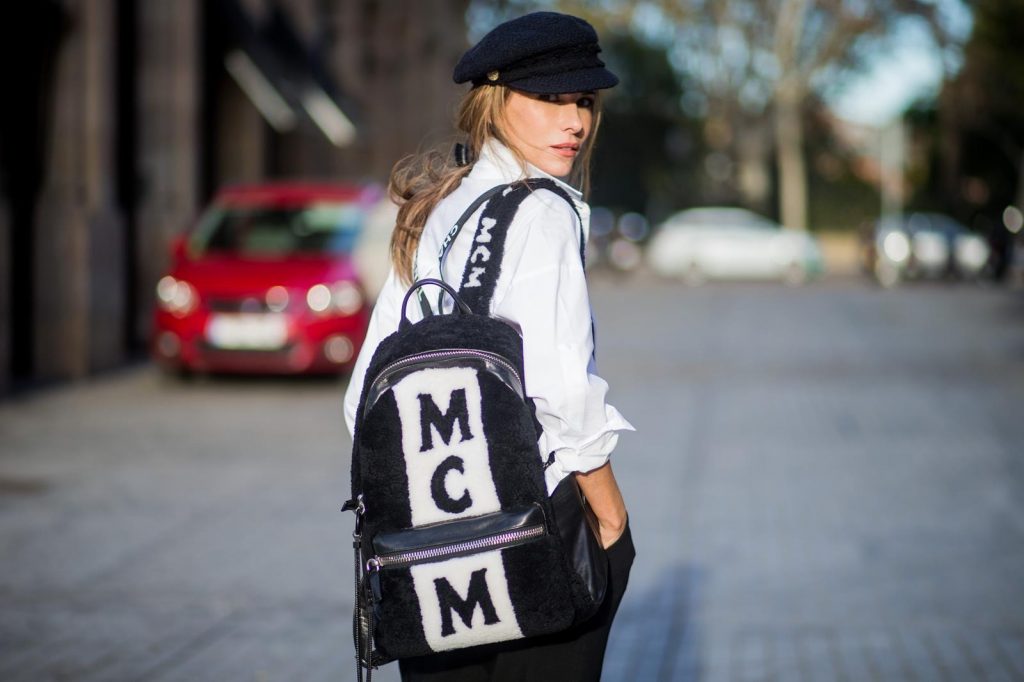Alexandra Lapp wearing black and white vintage Chanel suspenders with Chanel logo in black and white, a white oversized shirt from Steffen Schraut, black high waist pants from Zara, XL backpack in lambskin with black and white MCM logo and Chanel baker boy cap in black tweed and ballerinas in white with black tip and logo from Chanel on November 27, 2017 in Barcelona, Spain.