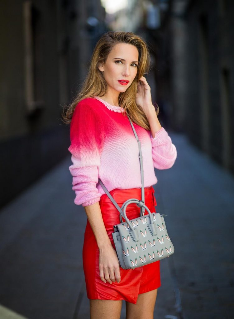 Alexandra Lapp wearing batik knit, a red leather mini skirt with integrated belt around the waist from Set Fashion, a batik cashmere pullover in pink and red from Heartbreaker, red satin pumps from Christian Louboutin with long satin bow, silver shadow colored MCM Milla Tote bag on November 27, 2017 in Barcelona, Spain.
