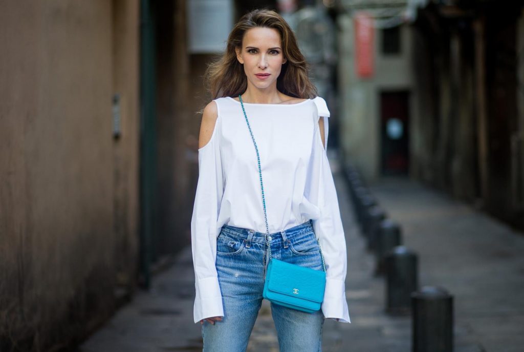 Street Style In Barcelona BARCELONA, SPAIN - NOVEMBER 29: Alexandra Lapp wearing white off-shoulder blouse and light blue lace coat with flowers from Steffen Schraut, silver mirrored sunglasses from Le Specs, multicolored Sophia Webster sandals heels, vintage Levis from ReDone and Chanel purse bag with a long golden strap and Chanel sign in front on November 29, 2017 in Barcelona, Spain.