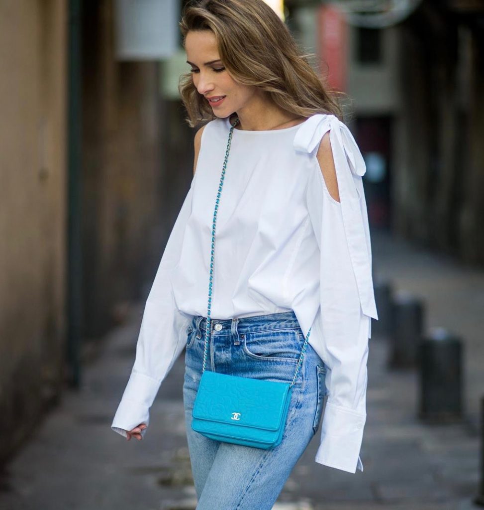 Street Style In Barcelona BARCELONA, SPAIN - NOVEMBER 29: Alexandra Lapp wearing white off-shoulder blouse and light blue lace coat with flowers from Steffen Schraut, silver mirrored sunglasses from Le Specs, multicolored Sophia Webster sandals heels, vintage Levis from ReDone and Chanel purse bag with a long golden strap and Chanel sign in front on November 29, 2017 in Barcelona, Spain.