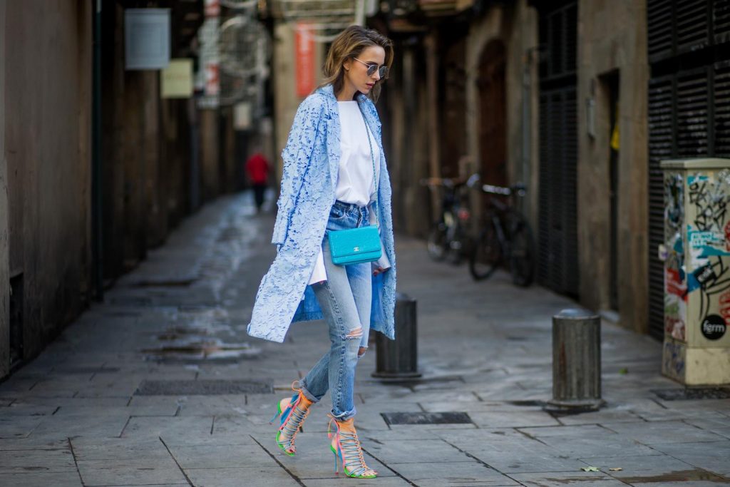 Street Style In Barcelona BARCELONA, SPAIN - NOVEMBER 29: Alexandra Lapp wearing white off-shoulder blouse and light blue lace coat with flowers from Steffen Schraut, silver mirrored sunglasses from Le Specs, multicolored Sophia Webster sandals heels, vintage Levis from ReDone and Chanel purse bag with a long golden strap and Chanel sign in front on November 29, 2017 in Barcelona, Spain.