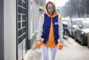 MILAN, ITALY - FEBRUARY 21: Alexandra Lapp wearing college style, a college jacket in blue, white and orange from MCM, an orange hoodie from glam-o-meter, white destroyed jeans from Frame a white Milla handbag from MCM, white pumps from Christian Louboutin and Ray-Ban sunglasses seen during Milan Fashion Week Fall/Winter 2018/19 on February 21, 2018 in Milan, Italy.