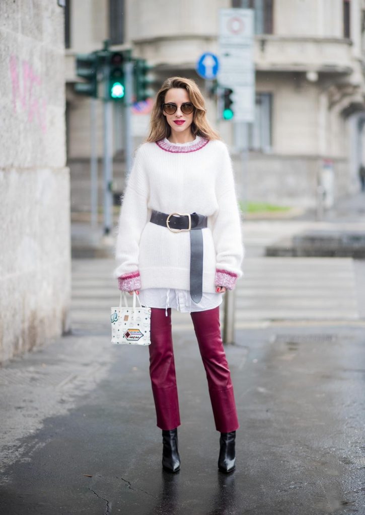 Alexandra Lapp wearing flared leather pants in bordeaux by Dorothee Schumacher, an off-white cotton pullover with a bordeaux colored neckline and a long white shirt with a waist line by Dorothee Schumacher, a long black leather belt with a big buckle by Dorothee Schumacher, black leather ankle boots by Gianvito Rossi, cat-eye sunglasses in black with a golden rim by Maison Masada and Anya mini shopper in victory patch from MCM seen during Milan Fashion Week Fall/Winter 2018/19 on February 24, 2018 in Milan, Italy.