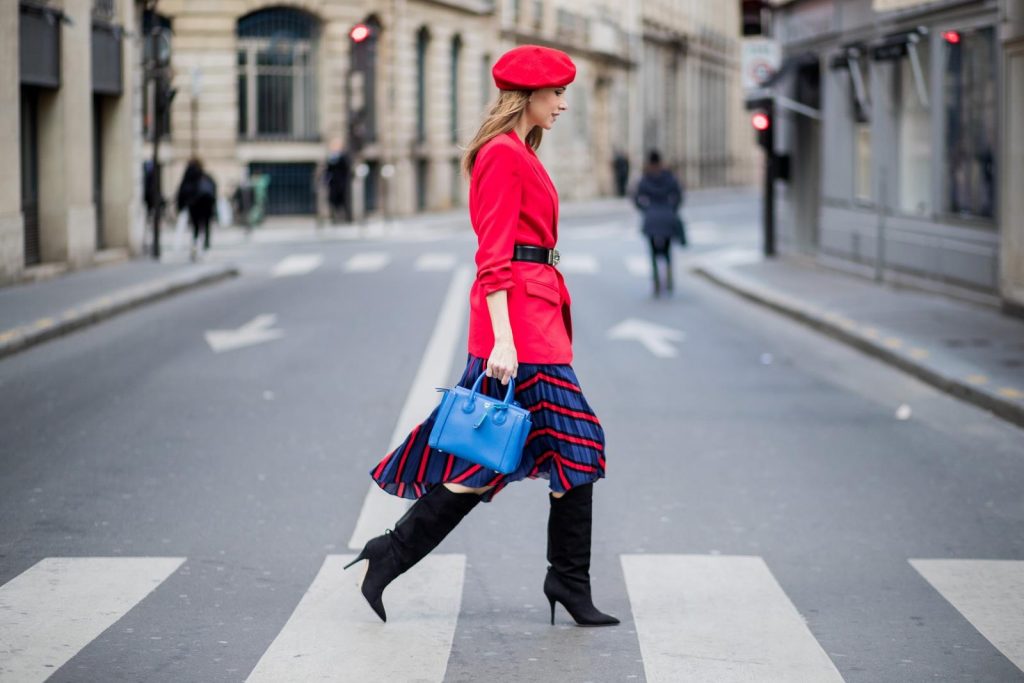 Alexandra Lapp wearing a long red blazer from Zara, a silk top from Jadicted, Collier de chien - a black waist belt with a silver buckle from Hermes, a blue Neo Milla handbag from MCM, a pleated skirt in blue with red stripes from H&M, black boots from Isabel Marant is seen on February 27, 2018 in Paris, France.