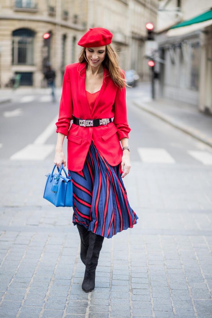 Alexandra Lapp wearing a long red blazer from Zara, a silk top from Jadicted, Collier de chien - a black waist belt with a silver buckle from Hermes, a blue Neo Milla handbag from MCM, a pleated skirt in blue with red stripes from H&M, black boots from Isabel Marant is seen on February 27, 2018 in Paris, France.