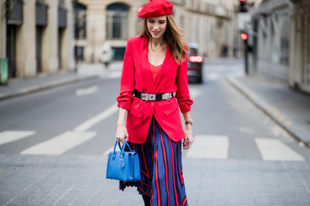 Alexandra Lapp wearing a long red blazer from Zara, a silk top from Jadicted, Collier de chien - a black waist belt with a silver buckle from Hermes, a blue Neo Milla handbag from MCM, a pleated skirt in blue with red stripes from H&M, black boots from Isabel Marant is seen on February 27, 2018 in Paris, France.