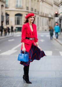 Alexandra Lapp wearing a long red blazer from Zara, a silk top from Jadicted, Collier de chien - a black waist belt with a silver buckle from Hermes, a blue Neo Milla handbag from MCM, a pleated skirt in blue with red stripes from H&M, black boots from Isabel Marant is seen on February 27, 2018 in Paris, France.