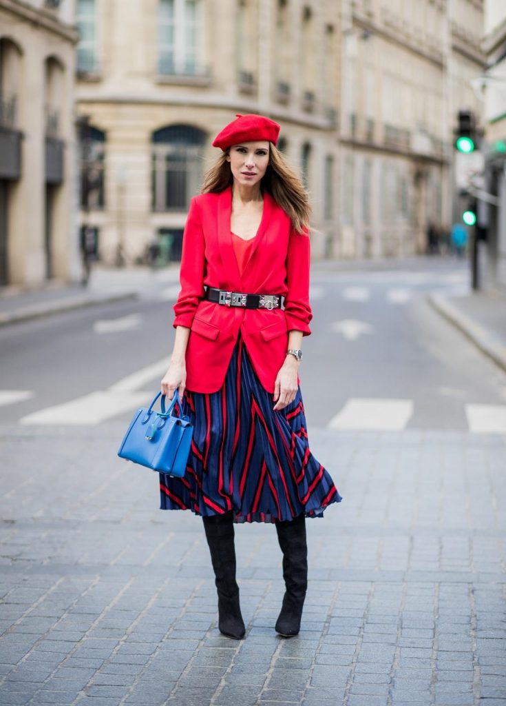 Alexandra Lapp wearing a long red blazer from Zara, a silk top from Jadicted, Collier de chien - a black waist belt with a silver buckle from Hermes, a blue Neo Milla handbag from MCM, a pleated skirt in blue with red stripes from H&M, black boots from Isabel Marant is seen on February 27, 2018 in Paris, France.