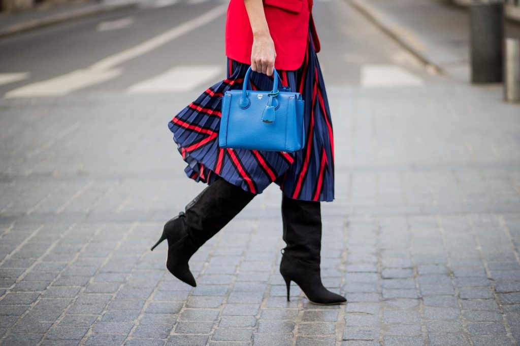 Alexandra Lapp wearing a long red blazer from Zara, a silk top from Jadicted, Collier de chien - a black waist belt with a silver buckle from Hermes, a blue Neo Milla handbag from MCM, a pleated skirt in blue with red stripes from H&M, black boots from Isabel Marant is seen on February 27, 2018 in Paris, France.