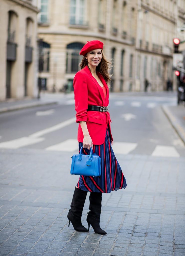 Alexandra Lapp wearing a long red blazer from Zara, a silk top from Jadicted, Collier de chien - a black waist belt with a silver buckle from Hermes, a blue Neo Milla handbag from MCM, a pleated skirt in blue with red stripes from H&M, black boots from Isabel Marant is seen on February 27, 2018 in Paris, France.