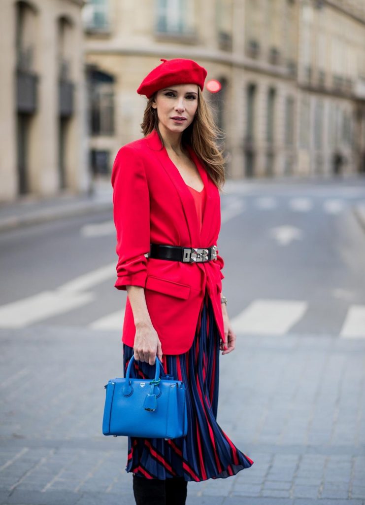 Alexandra Lapp wearing a long red blazer from Zara, a silk top from Jadicted, Collier de chien - a black waist belt with a silver buckle from Hermes, a blue Neo Milla handbag from MCM, a pleated skirt in blue with red stripes from H&M, black boots from Isabel Marant is seen on February 27, 2018 in Paris, France.