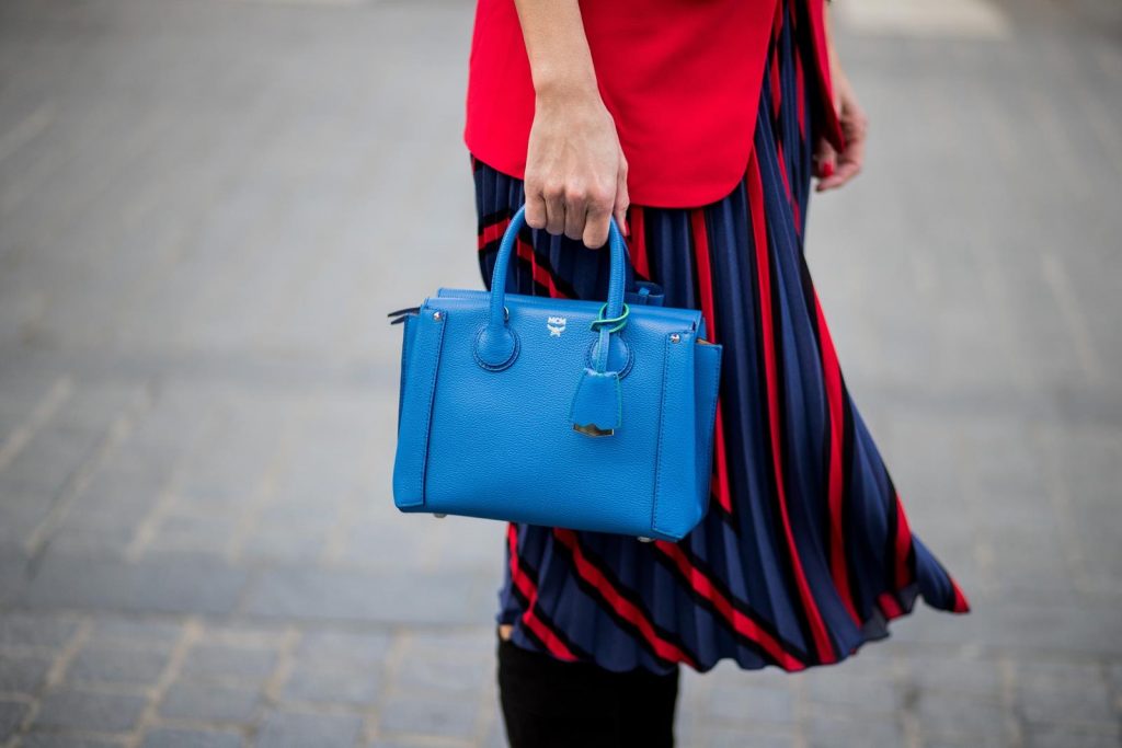 Alexandra Lapp wearing a long red blazer from Zara, a silk top from Jadicted, Collier de chien - a black waist belt with a silver buckle from Hermes, a blue Neo Milla handbag from MCM, a pleated skirt in blue with red stripes from H&M, black boots from Isabel Marant is seen on February 27, 2018 in Paris, France.