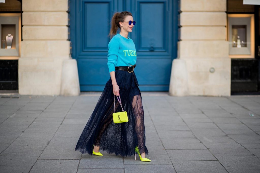 Alexandra Lapp wearing a turquoise pullover with a neon print Tuesday by Alberta Ferretti, a playful dress in black floral lace from Self-Portrait, black waist belt with big buckle from Dorothee Schumacher, blue mirrored sunglasses from Mykita, neon yellow pumps from Christian Louboutin and matching neon yellow handbag from Yves Saint Laurent is seen on February 28, 2018 in Paris, France.