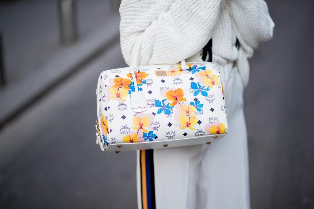 Alexandra Lapp wearing white sport pants with stripes on the side and a white knit v neck pullover from Zara, a white Baker Boy Cap from Chanel, suspenders from Chanel in white with black logo writing, black boots from Isabel Marant and Boston bag in floral print MCM is seen during Paris Fashion Week Womenswear Fall/Winter 2018/2019 on March 4, 2018 in Paris, France.