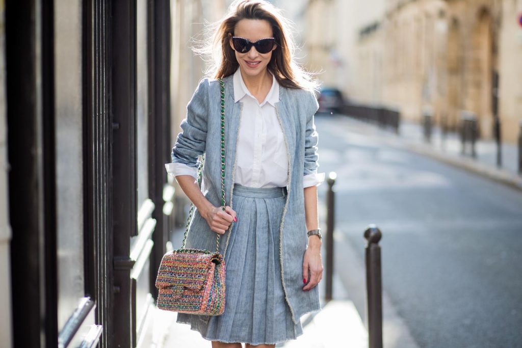 Alexandra Lapp in Linen Chic wearing a linen open front blazer with a fringed hem line in a denim optic and a high waist linen pleated skirt in denim optic and a fringed hem line by Steffen Schraut, a white blouse from Steffen Schraut, a 2.55 Chanel bag in multicolor, high heel sandals with a long satin bow with fruit motifs by Christian Louboutin and brown Chanel sunglasses with pearls seen on March 2, 2018 in Paris, France.