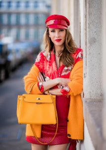 Alexandra Lapp wearing Hawaiian Silk Blouse in a kimono shape with all-over print by Jadicted, the Evangelista knitted cardigan by Ganni in turmeric orange, ruffled mini skirt in red leather by Magda Butrym, a Hermes Kelly bag in orange, Gianvito Rossi red patent pumps and gold mirrored Thom Browne sunglasses in red on May 6, 2018 in Duesseldorf, Germany.