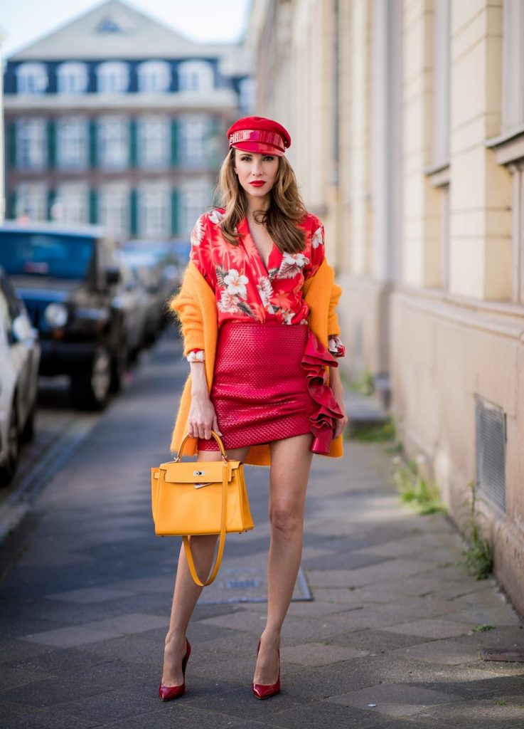 Alexandra Lapp wearing Hawaiian Silk Blouse in a kimono shape with all-over print by Jadicted, the Evangelista knitted cardigan by Ganni in turmeric orange, ruffled mini skirt in red leather by Magda Butrym, a Hermes Kelly bag in orange, Gianvito Rossi red patent pumps and gold mirrored Thom Browne sunglasses in red on May 6, 2018 in Duesseldorf, Germany.