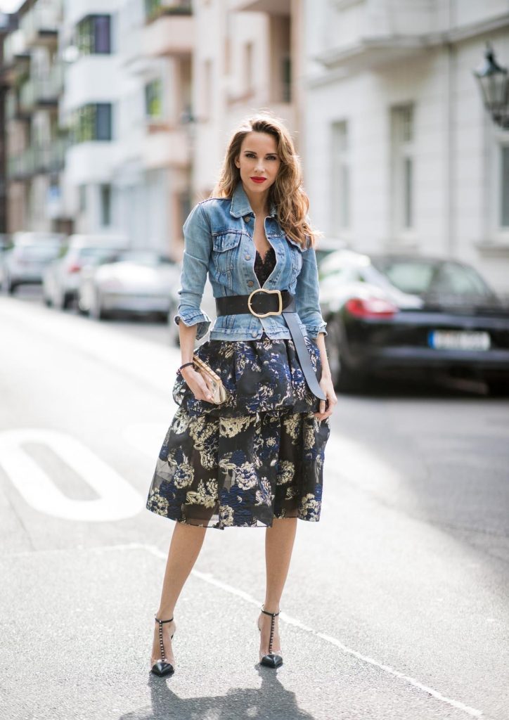 Alexandra Lapp wearing a Marchesa Notte dress with tiered corded lace and brocade in a mix of black, midnight-blue and gold by Marchesa Notte, blue trucker denim jacket by Levis, a gold buckle belt by Dorothee Schumacher, black Nosy t-bar Christian Louboutin sandals with a studded strap, handmade bracelet with rosegold fleur de lis lock by Coerlys and a vintage Chanel clutch in gold on May 3, 2018 in Duesseldorf, Germany.