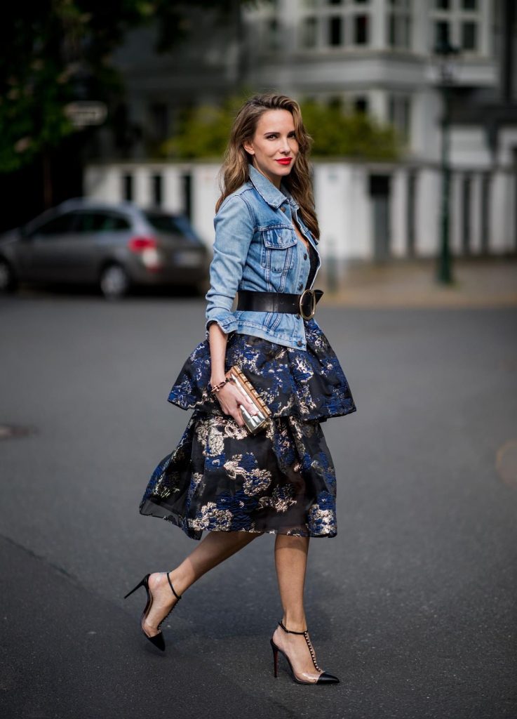 Alexandra Lapp wearing a Marchesa Notte dress with tiered corded lace and brocade in a mix of black, midnight-blue and gold by Marchesa Notte, blue trucker denim jacket by Levis, a gold buckle belt by Dorothee Schumacher, black Nosy t-bar Christian Louboutin sandals with a studded strap, handmade bracelet with rosegold fleur de lis lock by Coerlys and a vintage Chanel clutch in gold on May 3, 2018 in Duesseldorf, Germany.
