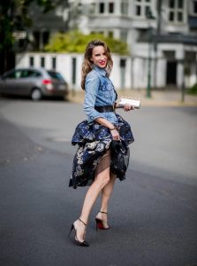 Alexandra Lapp wearing a Marchesa Notte dress with tiered corded lace and brocade in a mix of black, midnight-blue and gold by Marchesa Notte, blue trucker denim jacket by Levis, a gold buckle belt by Dorothee Schumacher, black Nosy t-bar Christian Louboutin sandals with a studded strap, handmade bracelet with rosegold fleur de lis lock by Coerlys and a vintage Chanel clutch in gold on May 3, 2018 in Duesseldorf, Germany.