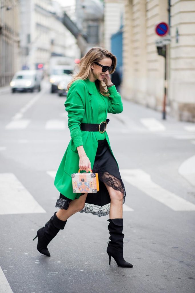 Alexandra Lapp wearing a lingerie look with a satin black skirt with lace around the rim from Zara, a green knit pullover from H&M, a black waist belt with large buckle from Dorothee Schumacher, black boots from Isabel Marant, a green light coat from Stella McCartney, black sunglasses from Celine and a cross body bag with crystal flowers from MCM is seen on February 27, 2018 in Paris, France.