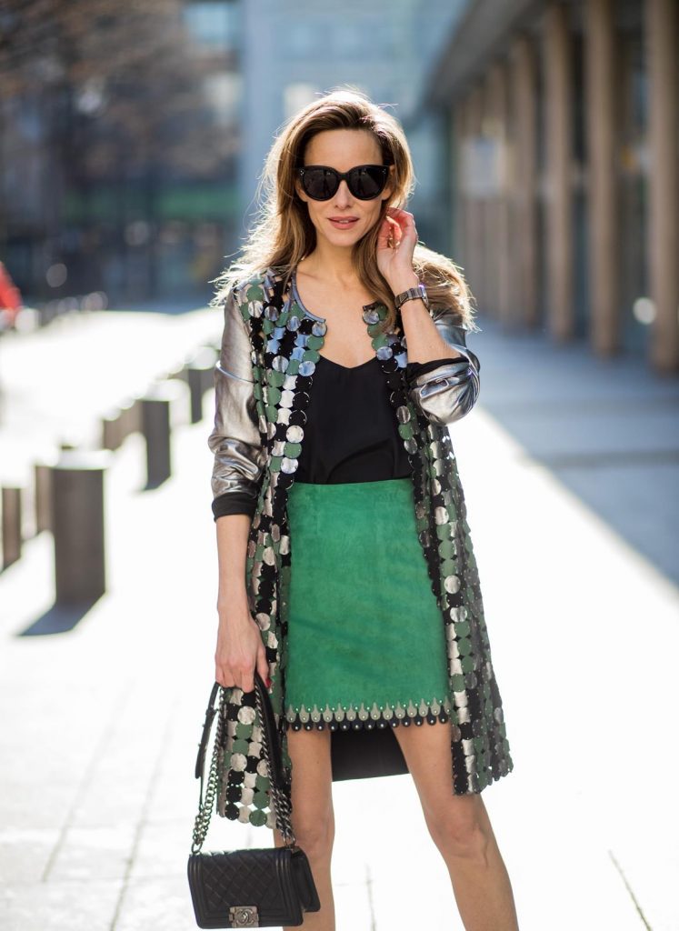 Alexandra Lapp wearing a silver coat from Yves Salomon with silver, green and black round leather parts with studs on the front, a short green suede leather skirt with blue and light grey pieces around the bottom line with studs by Yves Salomon, a black satin top from Jadicted, a black Chanel boy bag, black suede pumps by Christian Louboutin and black Celine sunglasses during Paris Fashion Week Womenswear Fall/Winter 2018/2019 on March 3, 2018 in Paris, France.