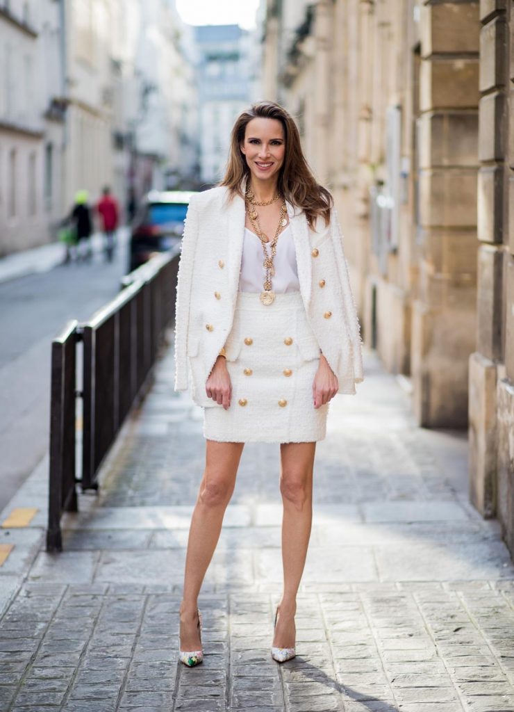 Alexandra Lapp in a full Balmain costume - a white tweed blazer with golden buttons and a matching tweed mini skirt with golden buttons both Balmain, a white silk top from Jadicted, heels from Christian Louboutin and Vintage necklaces from Chanel during Paris Fashion Week Womenswear Fall/Winter 2018/2019 on March 4, 2018 in Paris, France.