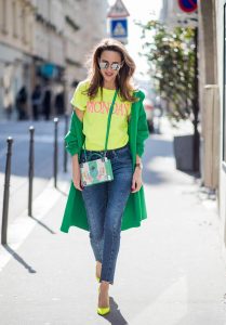 Alexandra Lapp in Mondays Statement Shirt Look wearing a yellow neon t-shirt with pink letters writing Monday by Alberta Ferretti, a blue pair of AG Jeans, a green coat from Stella McCartney, yellow neon pumps by Christian Louboutin, the Berlin cross body bag with crystal flowers from MCM and sunglasses by Le Specs during Paris Fashion Week Womenswear Fall/Winter 2018/2019 on March 5, 2018 in Paris, France.