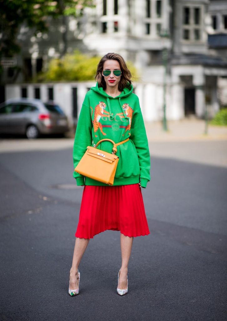 Alexandra Lapp in a Hermès Kelly Look wearing a green tiger print Gucci logo hoodie, a red pleated skirt by SET, a Hermes Birkin 30 bag in orange, Pigalle Follies pumps by Christian Louboutin and green mirrored Ray Ban sunglasses on May 3, 2018 in Duesseldorf, Germany. 