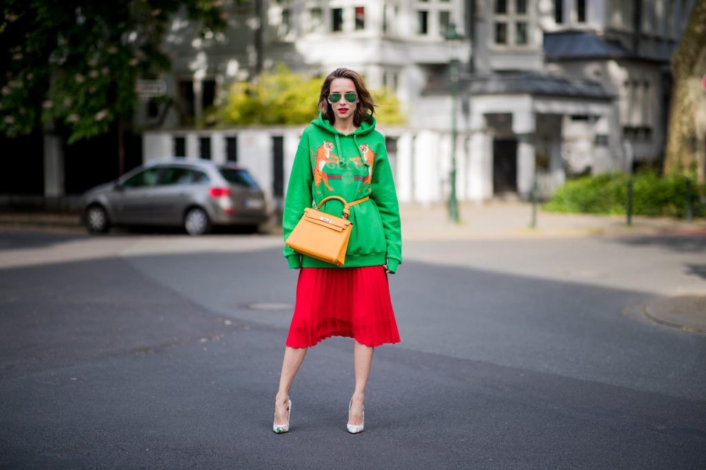 Alexandra Lapp in a Hermès Kelly Look wearing a green tiger print Gucci logo hoodie, a red pleated skirt by SET, a Hermes Birkin 30 bag in orange, Pigalle Follies pumps by Christian Louboutin and green mirrored Ray Ban sunglasses on May 3, 2018 in Duesseldorf, Germany. 