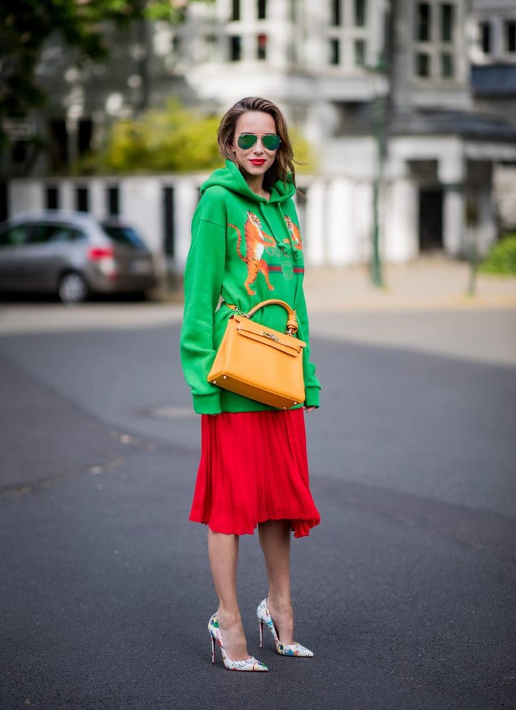 Alexandra Lapp in a Hermès Kelly Look wearing a green tiger print Gucci logo hoodie, a red pleated skirt by SET, a Hermes Birkin 30 bag in orange, Pigalle Follies pumps by Christian Louboutin and green mirrored Ray Ban sunglasses on May 3, 2018 in Duesseldorf, Germany. 